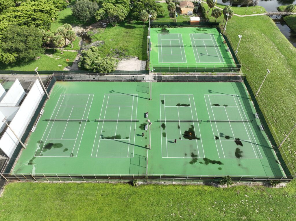 Aerial view of tennis courts with uneven green patches.