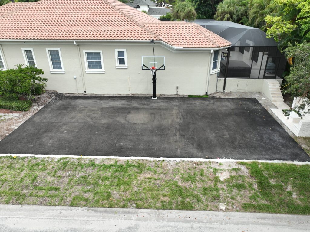 Freshly paved driveway in front of a beige house with a black lamp post.