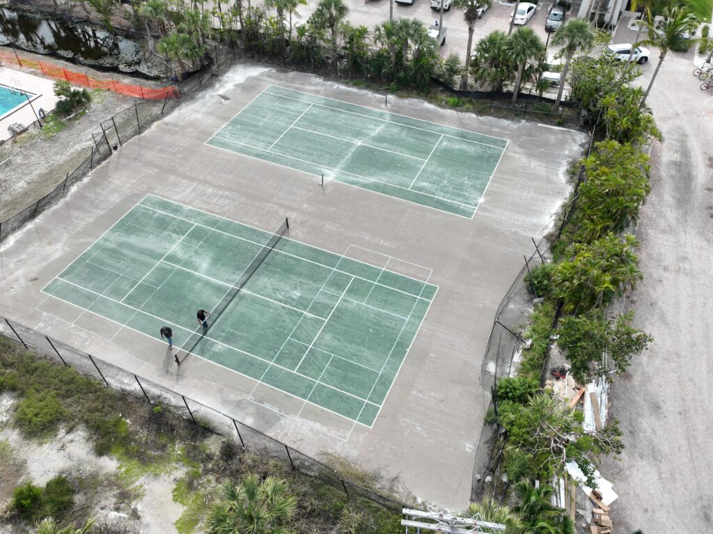 Aerial view of two outdoor tennis courts surrounded by trees and bushes.