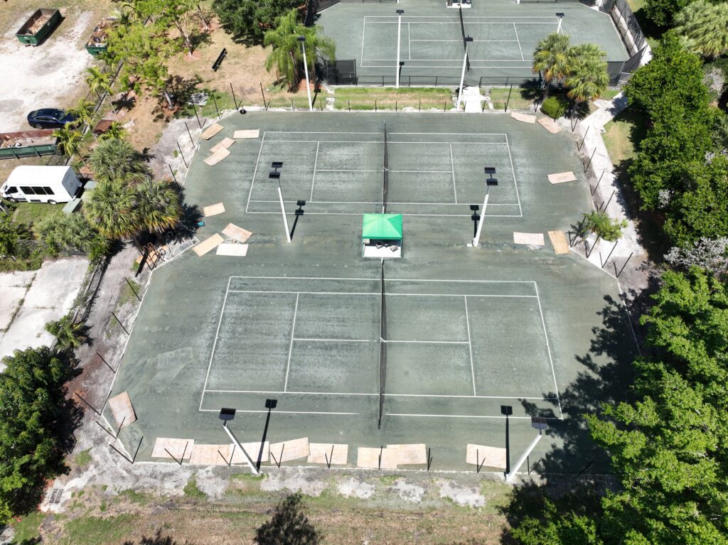 Aerial view of an empty, worn-out tennis court with faded lines and cracked surface.