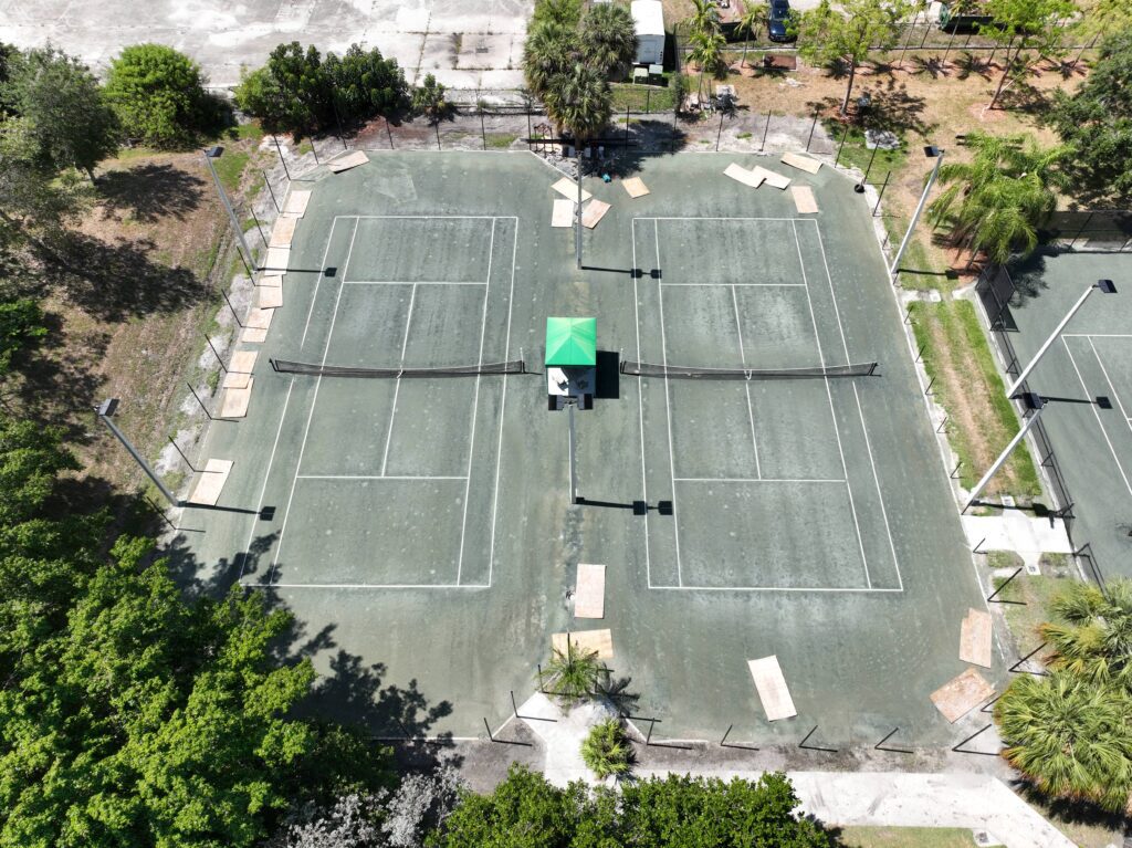 A worn-out outdoor tennis court surrounded by trees and greenery.