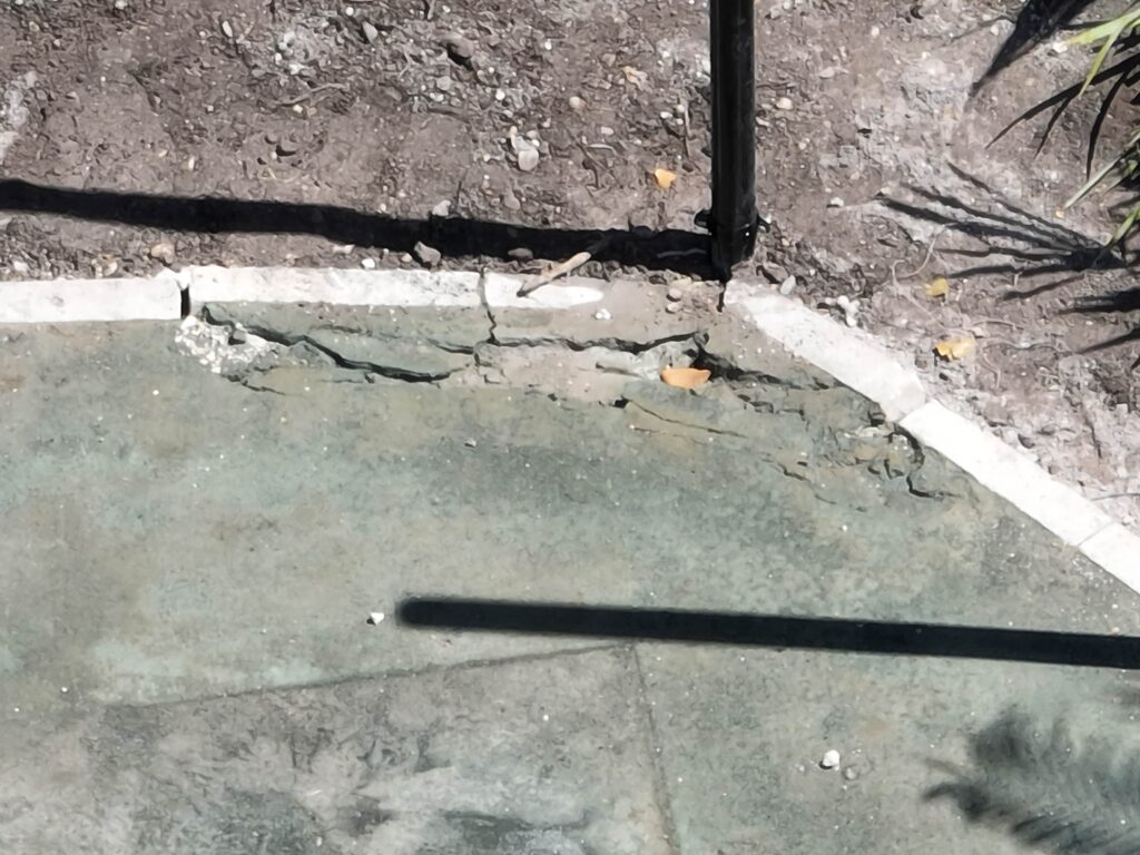 A close-up of a concrete surface with a shadow and a corner of a structure.