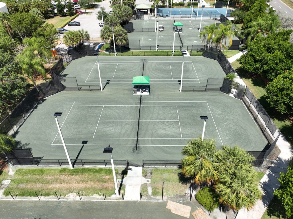 Aerial view of three adjacent tennis courts surrounded by greenery and buildings.