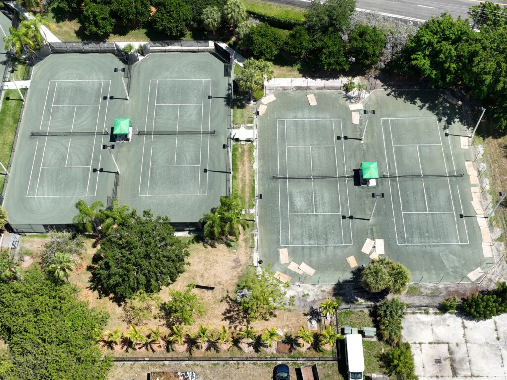 Aerial view of four tennis courts surrounded by trees and greenery.