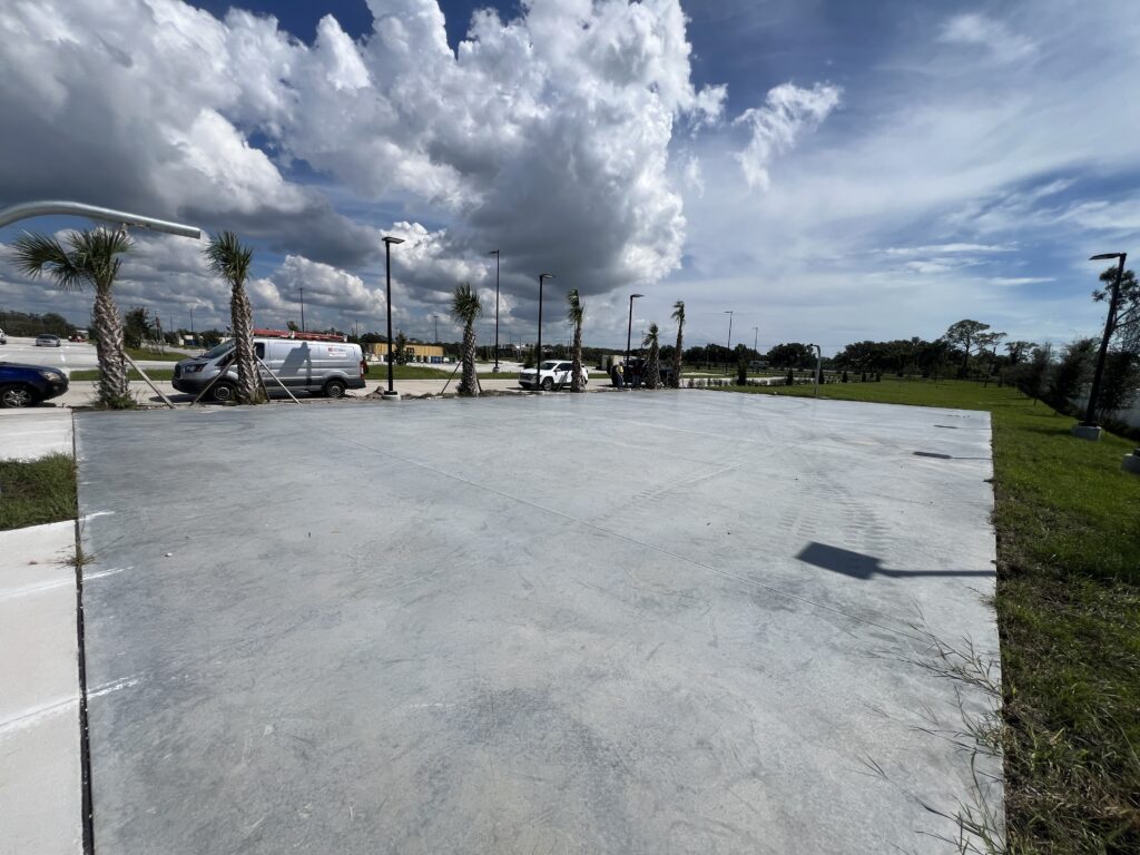 A large empty concrete area under a cloudy sky with some distant cranes.