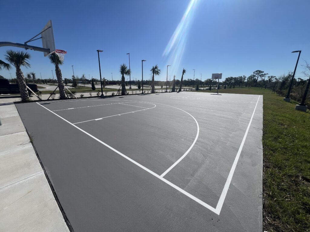 A sunny outdoor basketball court with clear markings and palm trees in the background.