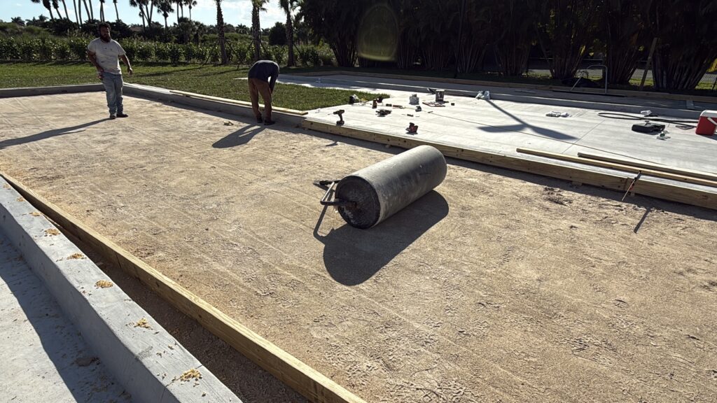 Worker using a roller to flatten a dirt surface outdoors.
