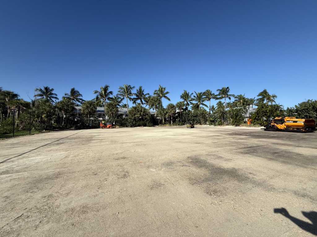A wide, open sandy area bordered by palm trees under a clear blue sky.