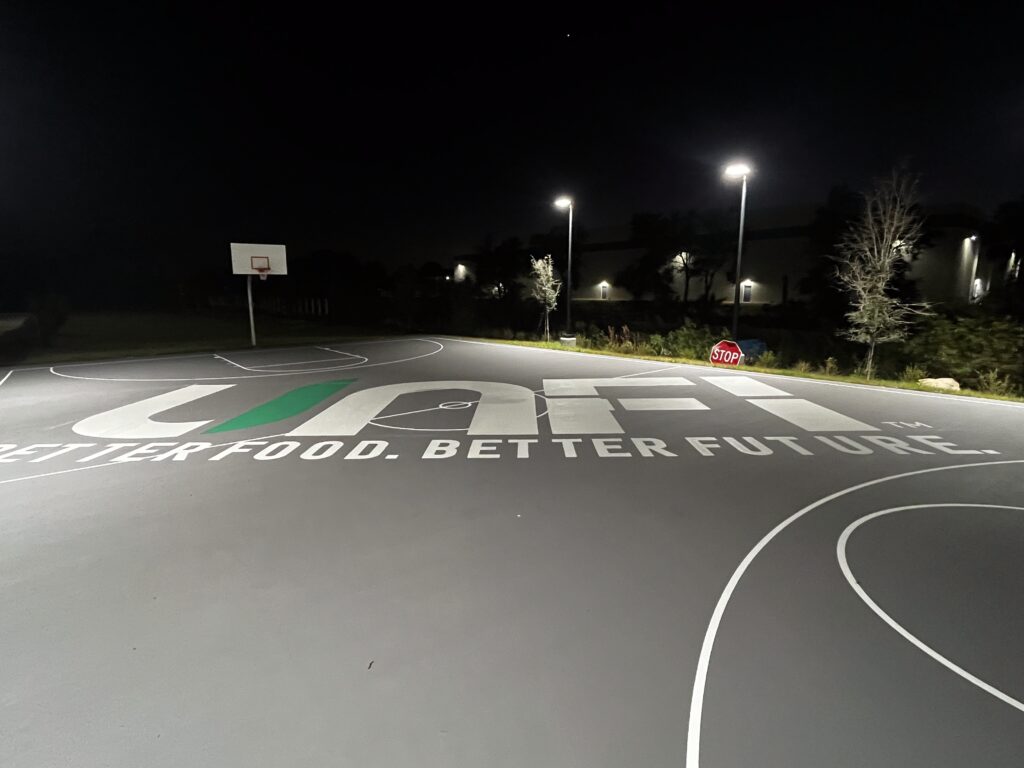 Nighttime view of an empty outdoor basketball court with bright lights.