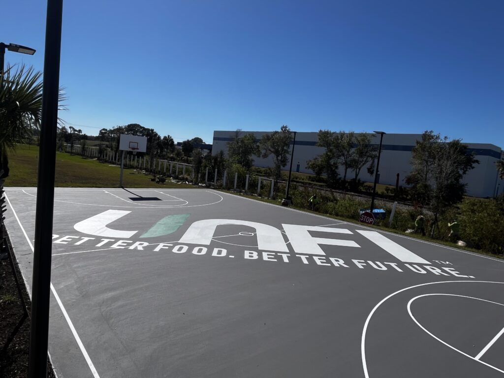 Outdoor basketball court with a large logo and clear blue sky.