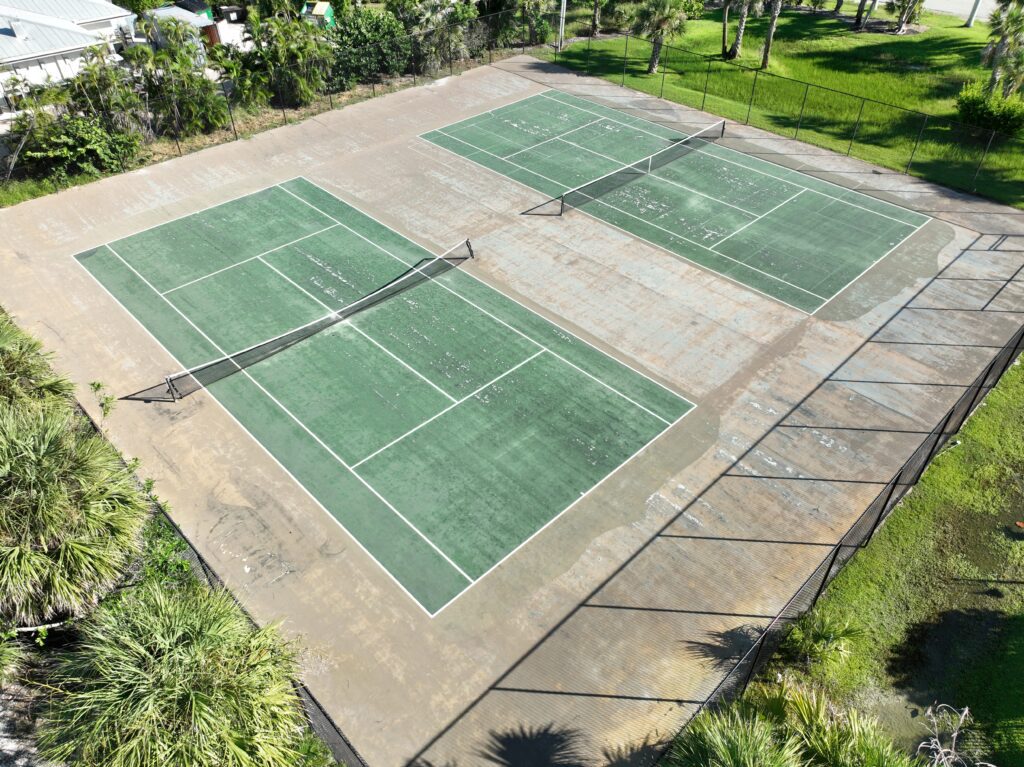 Empty outdoor pickleball courts surrounded by greenery on a sunny day.