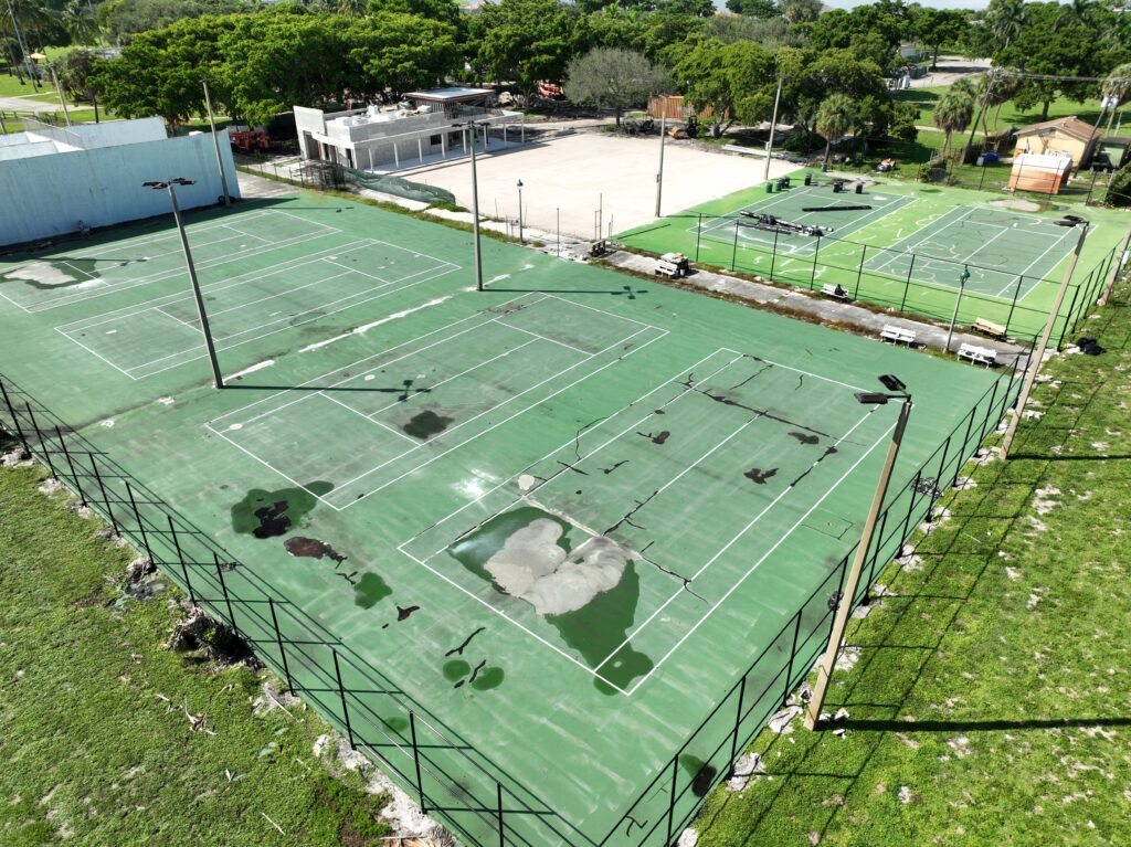 Aerial view of a worn-out tennis court with visible cracks and faded lines.