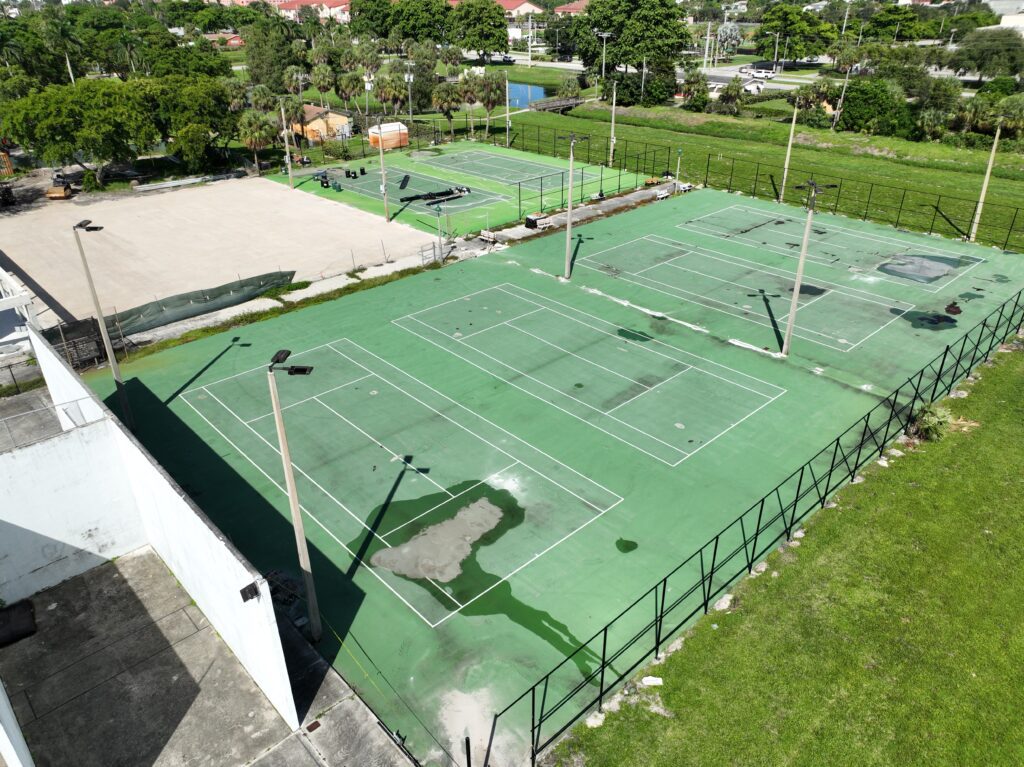 Outdoor tennis courts with green surface under sunlight.
