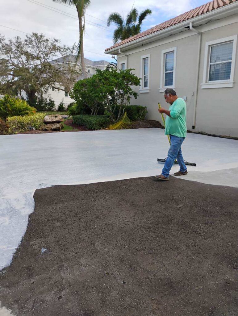 Man inspecting a freshly poured concrete slab beside a dirt patch.